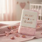 Protège carnet de santé bébé rose velours blanc brodé doré et fourrure rose poudre, posé sur couverture tricot rose avec nœud et pétales de roses - cadeau naissance fille
